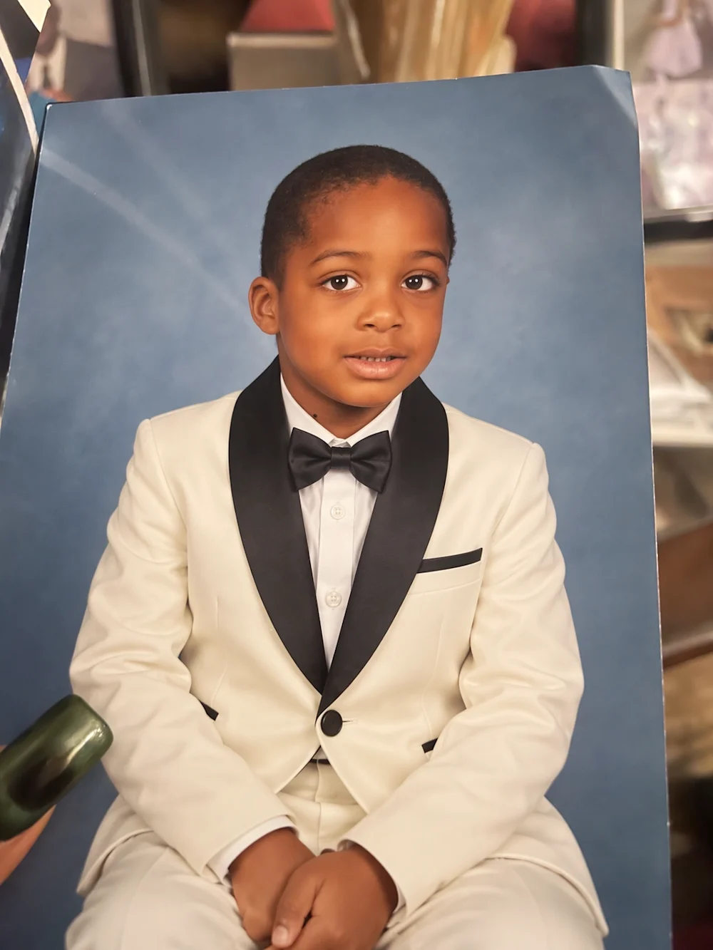 The same child wearing an ivory tuxedo and black bow tie, with the original pose and blue background